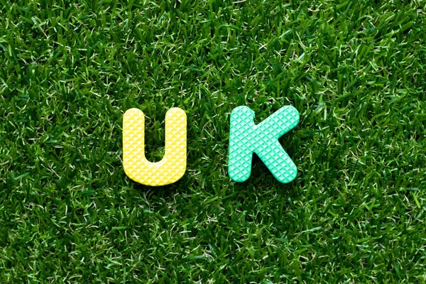 Brinquedo carta de espuma em palavra (abreviatura de reino unido) no fundo grama verde — Fotografia de Stock