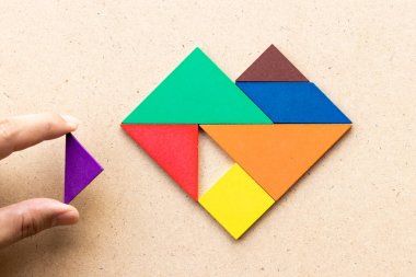 Ahşap arka plan üzerinde şekil yerine getirmek için üçgen parça beklemek kalp şeklinde Renk tangram bulmaca