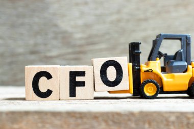 Toy forklift, ahşap arka planda CFO (Mali İşler Müdürü 'nün kısaltması) sözcüğünün tamamlanması için O harfi engelini tutar.
