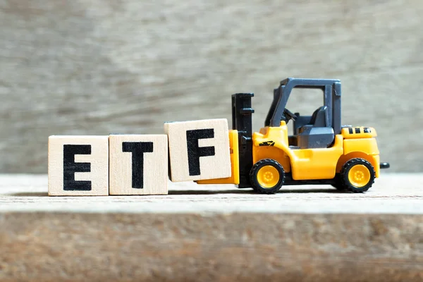 Spielzeuggabelstapler halten Buchstabenblock f, um das Wort etf (Abkürzung für Exchange Traded Fund) auf Holzgrund zu vervollständigen — Stockfoto