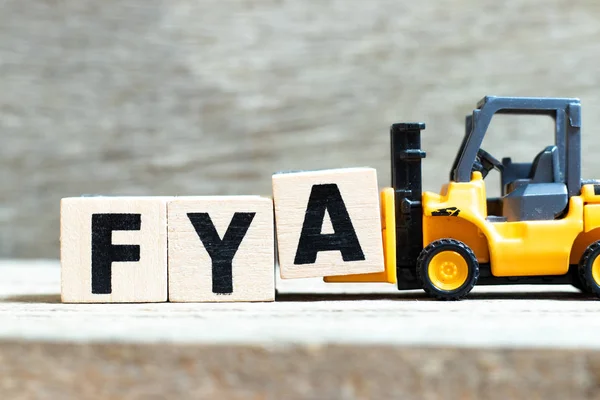 Speelgoed vorkheftruck houden letter blok A te voltooien woord Fya (afkorting van voor uw actie of aandacht) op houten achtergrond — Stockfoto
