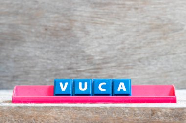 Tile letter on red rack in word VUCA (abbreviation of Volatility, uncertainty, complexity and ambiguity) on wood background clipart
