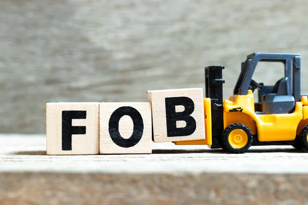 Toy vorkheftruck Hold letter blok B te voltooien woord fob (afkorting van Free on Board) op hout achtergrond — Stockfoto