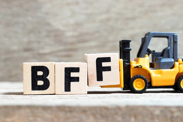 Spielzeuggabelstapler halten Buchstabenblock f, um das Wort BFF (Abkürzung für besten Freund für immer) auf Holzgrund zu vervollständigen — Stockfoto