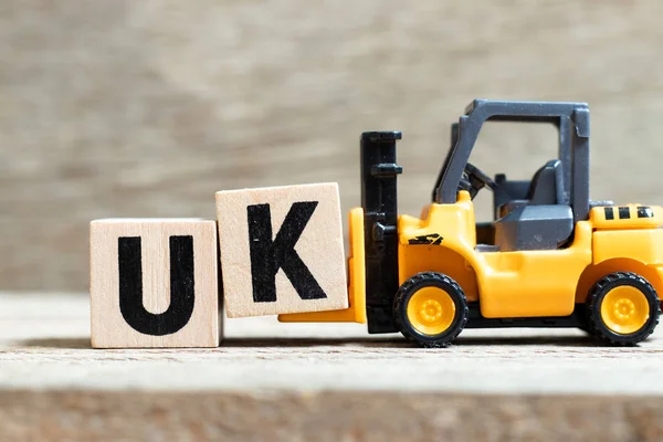 Toy vorkheftruck hold letter block k to complete word UK (afkorting van verenigd koninkrijk) on wood background — Stockfoto