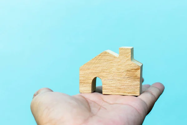 Mão segurar madeira modelo de bloco de casa com fundo de parede de concreto azul (Conceito para casa de sonho, realização da família ) — Fotografia de Stock