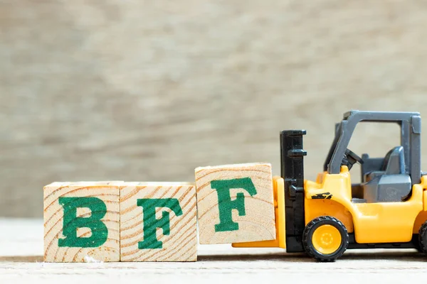 Toy forklift hold letter block f to complete word BFF (Abbreviation of best friend forever) on wood background
