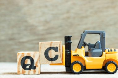 Tahta arkaplan üzerinde QC (Kalite Kontrolünün kısaltması) sözcüğünü tamamlamak için C harfi forklift engeli