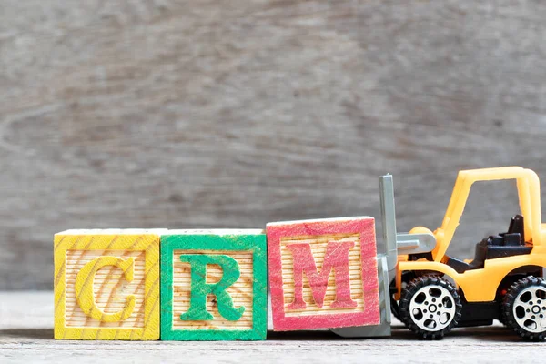 Toy forklift hold letter block M to complete word CRM (Abbreviation of Customer Relationship Management) on wood background