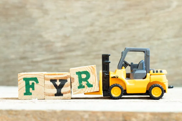 Toy forklift hold letter block R to complete word FYR (abbreviation of for your reference) on wood background