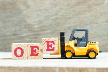 Oyuncak forklift harf bloğu E 'yi ahşap arkaplan üzerindeki OEE (genel ekipman etkinliğinin kısaltılması) sözcüğünü tamamlamak için tutun