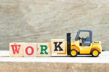 Oyuncak forklift harf bloğu k 'yi ahşap arkaplan çalışmasını tamamlamak için tutuyor
