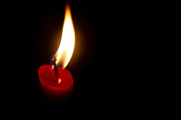 Red candle with yellow flame on black background