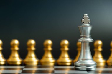 Gümüş kral satranç taşı siyah arka planda altın takım ile yüz yüze (Şirket stratejisi, iş kararı kavramı ve sorunla karşılaşma)