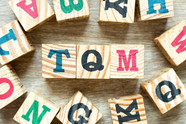 Kelime TQM ile alfabe harf bloğu (toplam kalite yönetiminin kısaltması) ve ahşap arkaplan üzerinde bir başkası