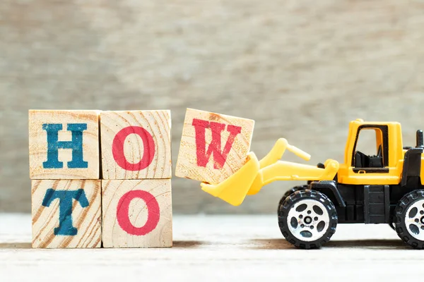 Toy bulldozer hold letter block w to complete word how to on wood background