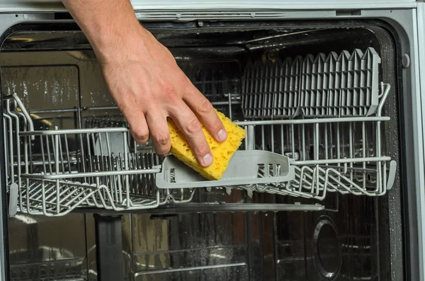 A man\'s hand cleans a dishwasher machine with a rag