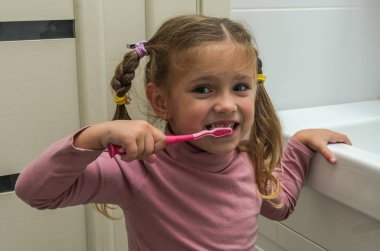 Girl child brushing her teeth with a toothbrush in the bathroom clipart