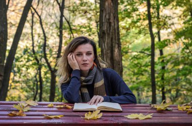 Sonbahar Park bir kitap okuma tahta bir masanın arkasında oturan genç güzel kız