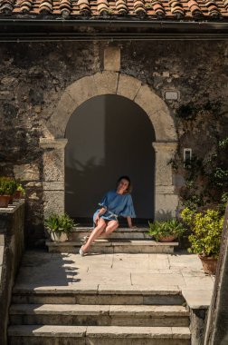 Genç bir kız için küçük bir İtalyan kasabasında eski antika evin girişine yakın basamaklarda oturur