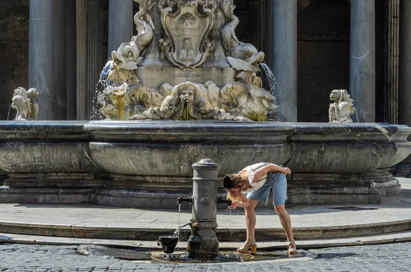 若い女の子の観光を魅力的なローマ イタリアの歴史的建造物の背景にローマ鼻のアンティーク水飲み場から水を飲む — ストック写真