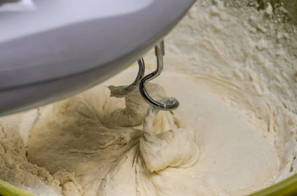 Cook kneads dough with electric mixers on the plate