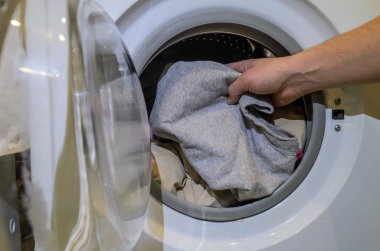 Bir adam kirli çamaşırları çamaşır makinesine koyar.