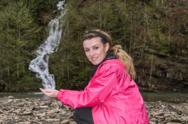 Bir dağ şelalesinin arka planında genç ve çekici bir turist kız.