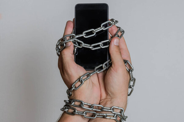 Смартфон мобильного телефона прикован цепями к рукам на светлом фоне
