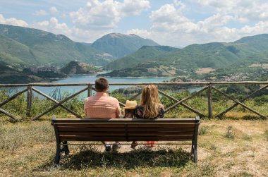 Anne, baba ve kızı göl Lago del Turano arka planda dağların arka planda bir bankta oturuyor - mutlu aile
