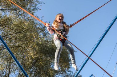 Lastik ipler üzerinde küçük sevimli kız bir lunaparkta trambolinde zıplıyor.