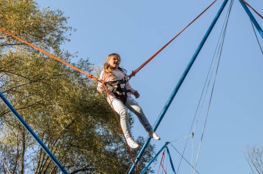 Lastik ipler üzerinde küçük sevimli kız bir lunaparkta trambolinde zıplıyor.