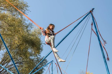 Lastik ipler üzerinde küçük sevimli kız bir lunaparkta trambolinde zıplıyor.