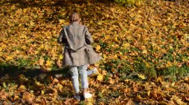 Genç ve çekici anne, sarı akçaağaç yaprakları arasında küçük kızını kollarında tutarak dönüyor. Mutlu bir aile.