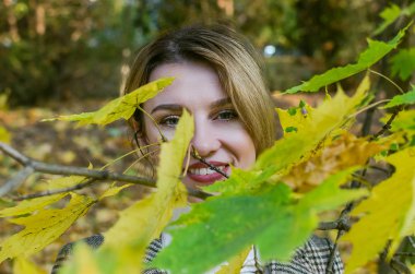 Sonbahar parkında, sarı akçaağaç yapraklarının arasında güneşli bir sonbahar gününde genç ve çekici bir kız.