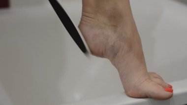 Kadın pedikür yapıyor. Banyoda ayağındaki yaşlı deriyi yüzüyor.