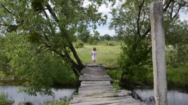 Genç ve çekici bir kız, küçük bir nehrin üzerindeki tahta bir köprüde yürüyor.