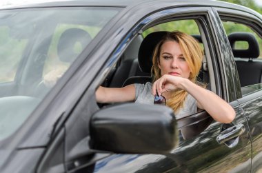 Genç ve çekici bir kız siyah bir arabanın direksiyonunda güneş gözlüğü takıyor.