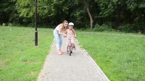 若い母親は彼女の娘に公園で自転車に乗ることを教えています — ストック動画