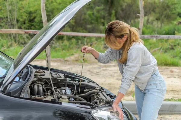 Young woman checking the oil level in the engine under the hood of a black car with a dipstick