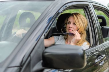 Genç ve çekici bir kız siyah bir arabanın direksiyonunda güneş gözlüğü takıyor.