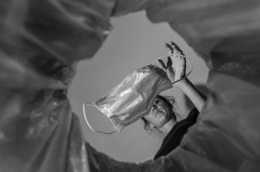 Kadın kullanılmış bir tıbbi maskeyi çöp kutusuna atıyor.