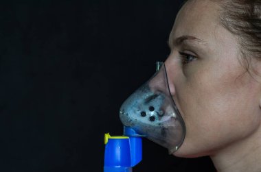 Kadın siyah arka planda nefes alırken maskenin içine nefes alıyor.