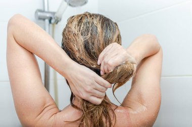 Genç ve güzel bir kız saçını şampuanla yıkıyor.