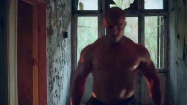 Çıplak gövdeli atletik bir adam terk edilmiş bir binada duruyor.