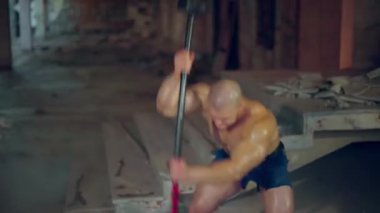 Atletik adam lastiğe çekiç darbesi uyguluyor.