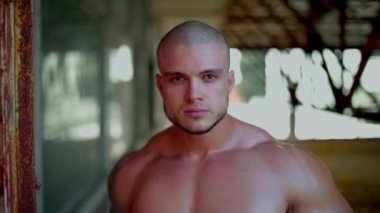 Elinde çekiçle çıplak gövdesi olan atletik bir adam yıkılmış bir binanın koridorunda duruyor.