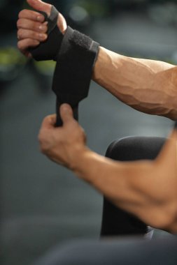 Adam bileğine bandaj sararak yoğun bir antrenman seansına hazırlanıyor. Bu etkinlik tutuş desteğini artırır ve spor salonunda egzersiz yaparken yaralanmaları önler.