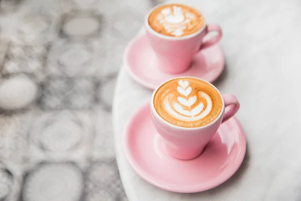 Mermer masa arka plan üzerinde güzel latte sanat ile kapuçino iki pembe bardak. — Stok fotoğraf