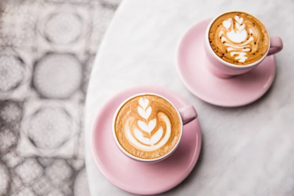 Two pink cups of cappuccino with beautiful latte art on marble table background. — Stock Photo, Image